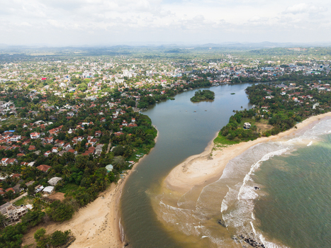 Aerial view of the Nilwala River mouth meeting the ocean with sandy beaches and urban rooftops surrounded by tropical greenery in Matara Southern Province Sri Lanka. Aerial view of the Nilwala River mouth meeting the ocean with sandy beaches and urban rooftops surrounded by tropical greenery in Matara Southern Province Sri Lanka.