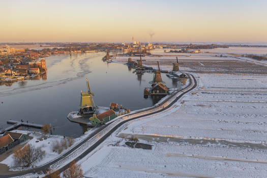 Aerial view of Zaanse Schans with traditional windmills along the riverbank snow covered fields and golden hour light in Zaandam Noord Holland Netherlands. Aerial view of Zaanse Schans with traditional windmills along the riverbank snow covered fields and golden hour light in Zaandam Noord Holland Netherlands.