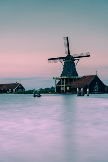 View of Zaanse Schans Windmill standing by the calm water under a soft pink and blue twilight sky with traditional wooden houses Zaandam Noord Holland Netherlands. View of Zaanse Schans Windmill standing by the calm water under a soft pink and blue twilight sky with traditional wooden houses Zaandam Noord Holland Netherlands.