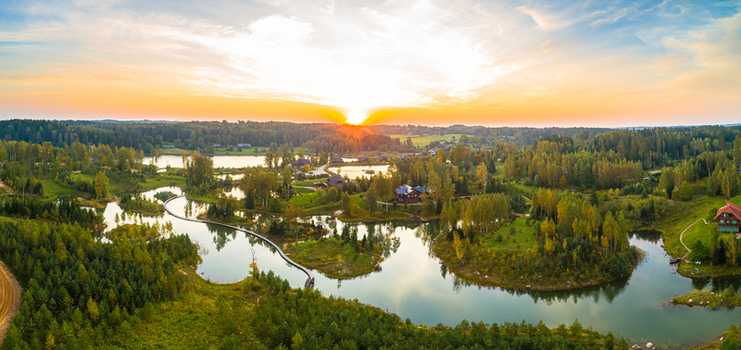 Aerial view of a serene lake surrounded by lush autumn forests and wooden cabins during a golden sunset in Latvia. Aerial view of a serene lake surrounded by lush autumn forests and wooden cabins during a golden sunset in Latvia.