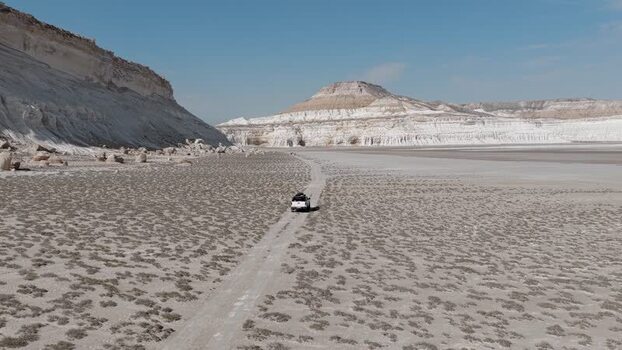 Aerial view of a vehicle driving through the Tuzbair salt flats Kazakhstan.