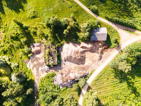 Aerial view of a rural site with piles of soil and debris near a small building surrounded by lush green trees and a dirt road in Salgale parish Jelgava Municipality Latvia. Aerial view of a rural site with piles of soil and debris near a small building surrounded by lush green trees and a dirt road in Salgale parish Jelgava Municipality Latvia.