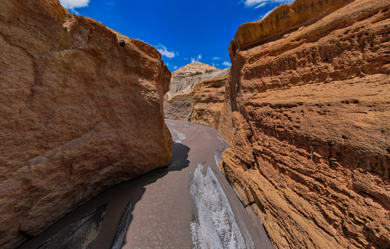 Aerial view of a river flowing through a deep canyon with steep eroded rock walls under a bright blue sky in Nepal.