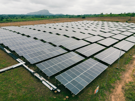 Aerial view of a large solar farm with rows of photovoltaic panels set in a rural landscape with a distant hill in Ogun State Nigeria.