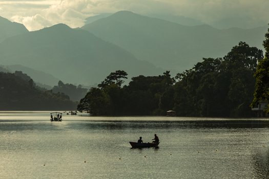 Pokhara Nepal 31 July 2026 View of a small boat with people on Phewa Lake surrounded by lush hills and mountains under a soft sky.