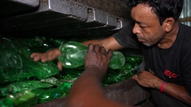 View of a worker recycling green plastic bottles in Bangladesh. View of a worker recycling green plastic bottles in Bangladesh.