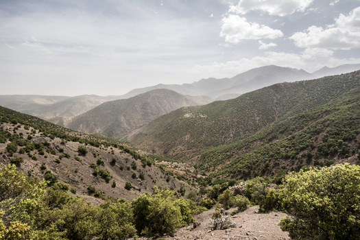 View of the lush valley and rugged slopes of the High Atlas mountains with green vegetation and hazy peaks in an arid landscape Tizi Oussem Marrakech Safi Morocco. View of the lush valley and rugged slopes of the High Atlas mountains with green vegetation and hazy peaks in an arid landscape Tizi Oussem Marrakech Safi Morocco.