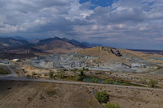 Aerial view of an open pit quarry with gravel piles mining equipment and conveyor belts set against rolling hills and mountains under a cloudy sky in Golden Colorado United States.