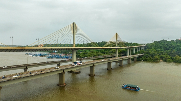 Aerial view of the Atal Setu cable stayed bridge spanning the Mandovi River with traffic a small boat navigating the water and lush green banks in Panaji Goa India.