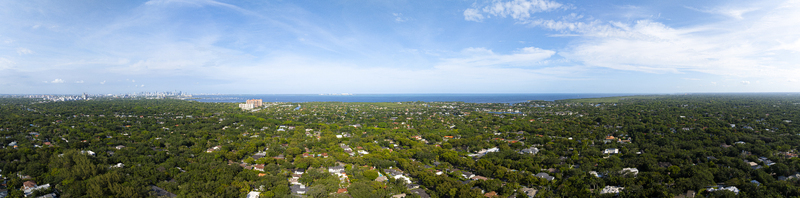 Aerial view of lush residential neighborhoods with dense tree canopies and rooftops stretching towards the ocean horizon in Coral Gables Florida United States.
