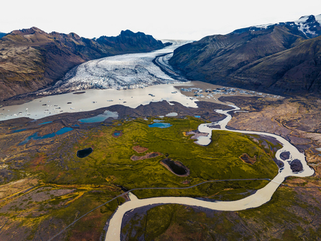 Aerial view of a glacier tongue flowing into a glacial lagoon with floating icebergs surrounded by mossy green volcanic terrain and a winding river in Iceland. Aerial view of a glacier tongue flowing into a glacial lagoon with floating icebergs surrounded by mossy green volcanic terrain and a winding river in Iceland.