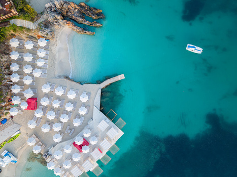 Aerial view of a beach resort with white umbrellas sunbeds and a wooden pier along turquoise waters in Ksamil Vlore County Albania. Aerial view of a beach resort with white umbrellas sunbeds and a wooden pier along turquoise waters in Ksamil Vlore County Albania.