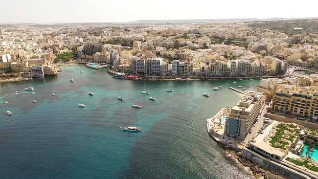 Aerial view of the coastal bay with boats anchored in turquoise water surrounded by dense urban architecture and hotels in Malta. Aerial view of the coastal bay with boats anchored in turquoise water surrounded by dense urban architecture and hotels in Malta.