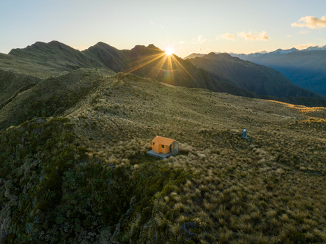 Aerial view of a solitary cabin nestled amongst tussock grass covered mountains as the sun bursts over the peaks Lake Kaniere West Coast Region New Zealand. Aerial view of a solitary cabin nestled amongst tussock grass covered mountains as the sun bursts over the peaks Lake Kaniere West Coast Region New Zealand.