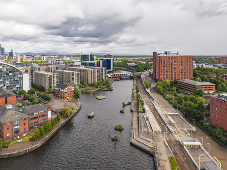 Aerial view of the Manchester Ship Canal featuring modern apartment buildings a tram station and a bridge under a cloudy sky in Stretford England United Kingdom.