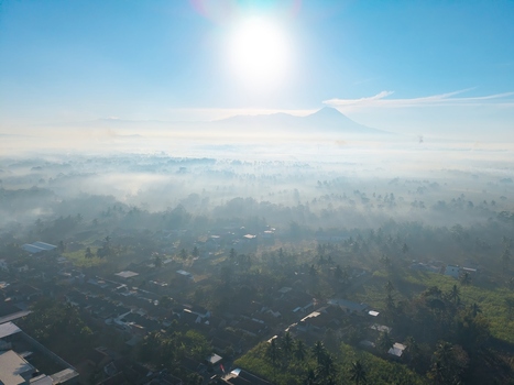 Aerial view of the town of Kepanjen nestled in a valley with morning mist lush greenery and a distant mountain under a bright sun in Kepanjen East Java Indonesia. Aerial view of the town of Kepanjen nestled in a valley with morning mist lush greenery and a distant mountain under a bright sun in Kepanjen East Java Indonesia.
