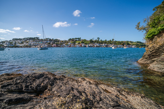 View of the Fowey River with moored sailboats historic town buildings along the waterfront and rocky shoreline under a clear blue sky in Fowey Cornwall United Kingdom. View of the Fowey River with moored sailboats historic town buildings along the waterfront and rocky shoreline under a clear blue sky in Fowey Cornwall United Kingdom.