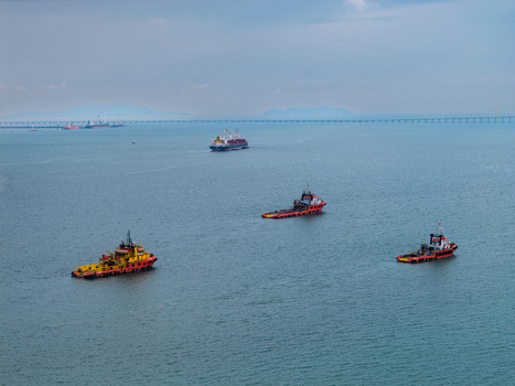 George Town Penang Malaysia 22 September 2026 Aerial view of tugboats navigating the waters near the Penang Bridge with a cargo ship in the distance under a cloudy sky. George Town Penang Malaysia 22 September 2026 Aerial view of tugboats navigating the waters near the Penang Bridge with a cargo ship in the distance under a cloudy sky.