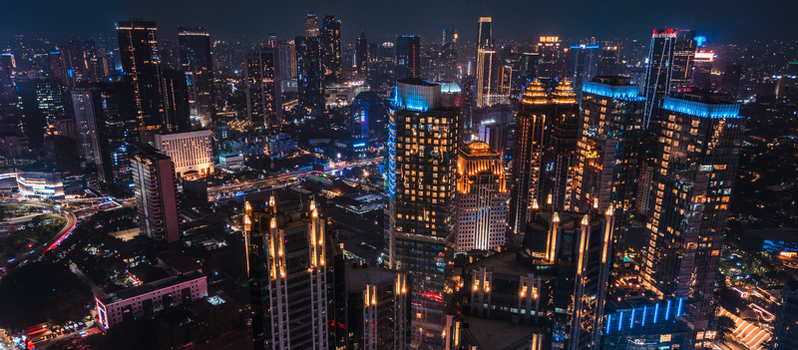Aerial view of the illuminated Jakarta skyline at night featuring modern skyscrapers glowing office towers and busy city streets in Jakarta Indonesia.