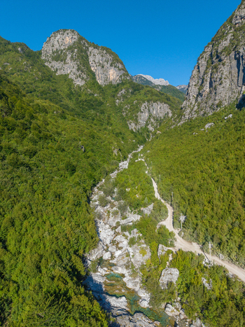 Aerial view of Blue Eye Theth featuring a turquoise stream winding through a rocky canyon surrounded by dense green forests and towering mountain peaks in Theth Shkoder County Albania. Aerial view of Blue Eye Theth featuring a turquoise stream winding through a rocky canyon surrounded by dense green forests and towering mountain peaks in Theth Shkoder County Albania.