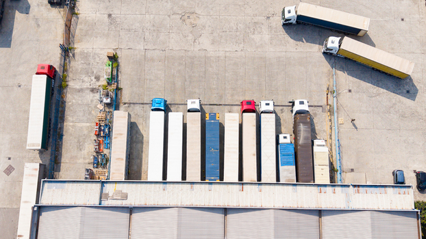 Aerial view of semi trucks and trailers parked at a distribution center loading dock with concrete yard in San Giuliano Milanese Lombardy Italy. Aerial view of semi trucks and trailers parked at a distribution center loading dock with concrete yard in San Giuliano Milanese Lombardy Italy.