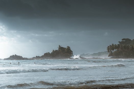 View of a stormy beach with crashing waves dark clouds and palm trees along the coastline in Costa Rica.