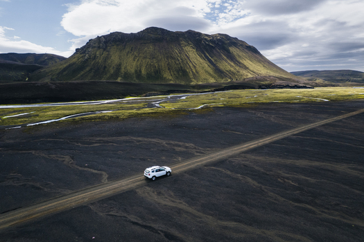 Aerial view of a white SUV driving on the F235 road through a vast volcanic landscape with black sand and mossy mountains Highlands of Iceland Iceland. Aerial view of a white SUV driving on the F235 road through a vast volcanic landscape with black sand and mossy mountains Highlands of Iceland Iceland.