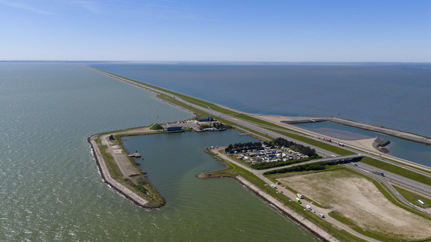Aerial view of Breezanddijk an artificial island and harbor along the Afsluitdijk causeway with a road and calm waters under a clear blue sky in Breezanddijk Friesland Netherlands.