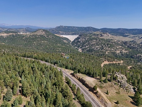 Aerial view of a dam nestled in the mountains with railroad tracks winding through a dense pine forest under a clear blue sky in Golden Colorado United States. Aerial view of a dam nestled in the mountains with railroad tracks winding through a dense pine forest under a clear blue sky in Golden Colorado United States.