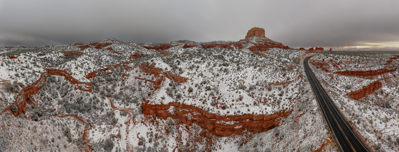 Aerial view of snow covered red rock mesas and deep canyons along a winding desert road under a dramatic overcast sky Page Arizona United States.