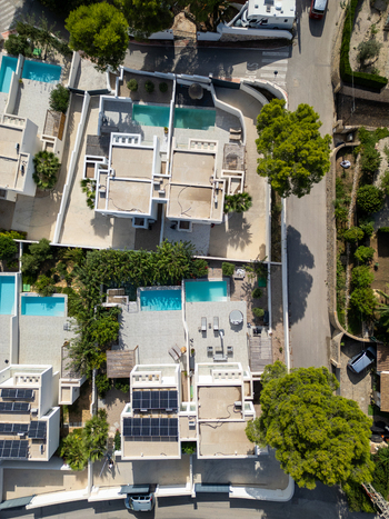 Aerial view of modern residential villas with private swimming pools solar panels on rooftops and lush green trees in Moraira Valencian Community Spain.