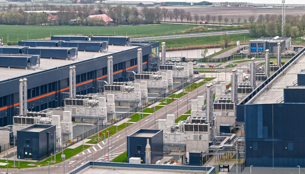 Aerial view of a modern data center campus featuring large industrial buildings and rows of back up energy generators surrounded by green fields Middenmeer Noord Holland Netherlands.