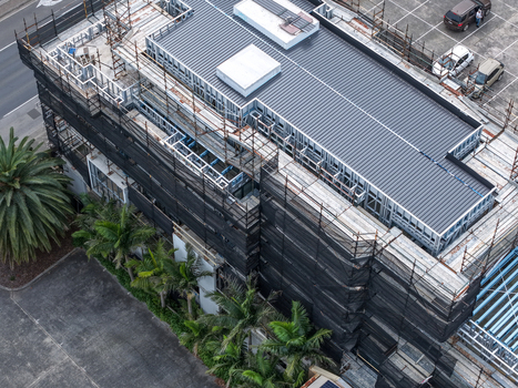 Melbourne VIC Australia 25 September 2026 Aerial view of a building under construction wrapped in black scaffolding featuring a metal roof palm trees and parking area.
