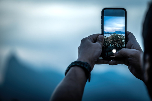 View of a person holding a smartphone to capture the landscape with Christ the Redeemer statue and lush mountains in Rio de Janeiro Rio de Janeiro Brazil.