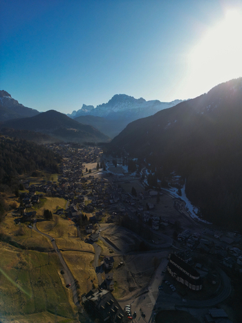 Aerial view of the alpine village of Pie Falcade nestled in a valley surrounded by the majestic snow capped peaks of the Dolomites under a bright sun Pie Falcade Veneto Italy.