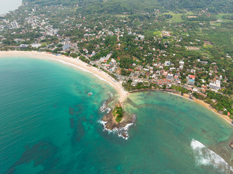 Aerial view of Parrot Rock and the sandy shoreline of Mirissa Beach with turquoise ocean water and lush tropical vegetation in Mirissa Southern Province Sri Lanka. Aerial view of Parrot Rock and the sandy shoreline of Mirissa Beach with turquoise ocean water and lush tropical vegetation in Mirissa Southern Province Sri Lanka.