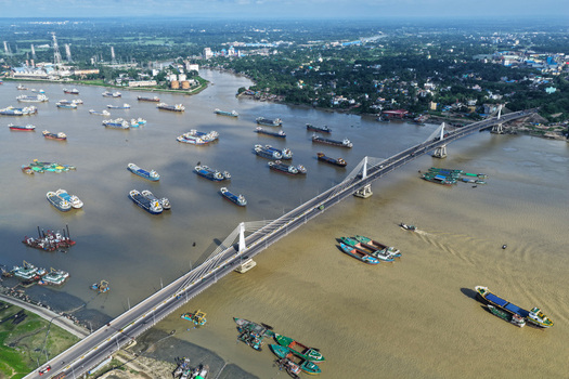 Aerial view of the Shah Amanat Bridge spanning the Karnaphuli River with numerous cargo ships and boats navigating the waterway in Chattogram Chittagong Division Bangladesh.