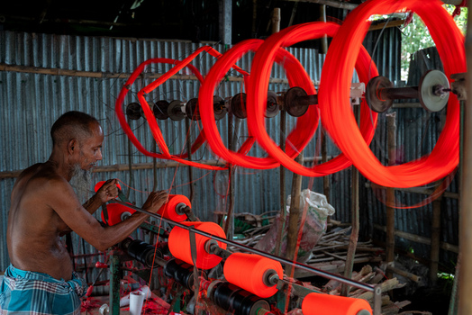 Joypurhat Rajshahi Division Bangladesh 22 September 2026 View of a man working with bright orange yarn on a textile machine in a workshop with corrugated metal walls. Joypurhat Rajshahi Division Bangladesh 22 September 2026 View of a man working with bright orange yarn on a textile machine in a workshop with corrugated metal walls.