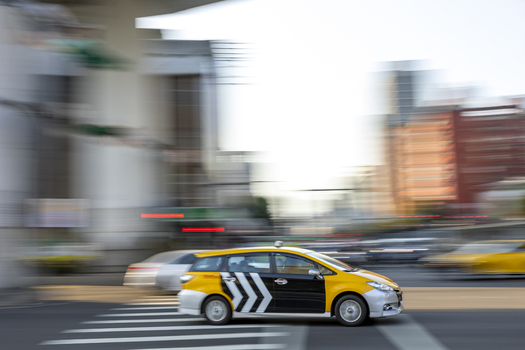 View of a yellow and black taxi cab driving with motion blur on a city street with a crosswalk in Taipei City Taiwan. View of a yellow and black taxi cab driving with motion blur on a city street with a crosswalk in Taipei City Taiwan.