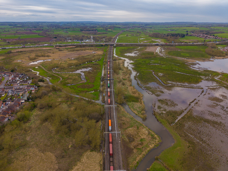 Aerial view of Doxey Marshes featuring a freight train moving along the railway tracks through the wetlands and green fields in Stafford England United Kingdom. Aerial view of Doxey Marshes featuring a freight train moving along the railway tracks through the wetlands and green fields in Stafford England United Kingdom.