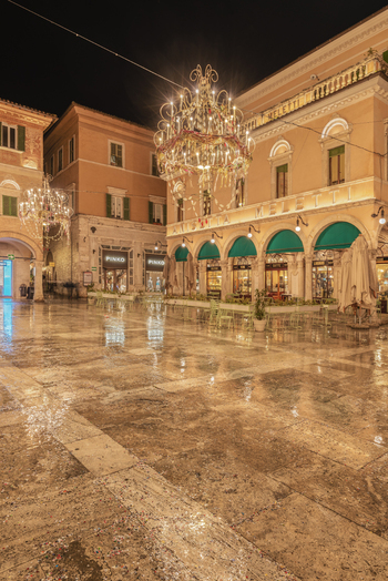Ascoli Piceno Italy 01 March 2025 View of Caffe Meletti in the historic Piazza del Popolo at night featuring ornate chandeliers wet stone pavement and elegant architecture.