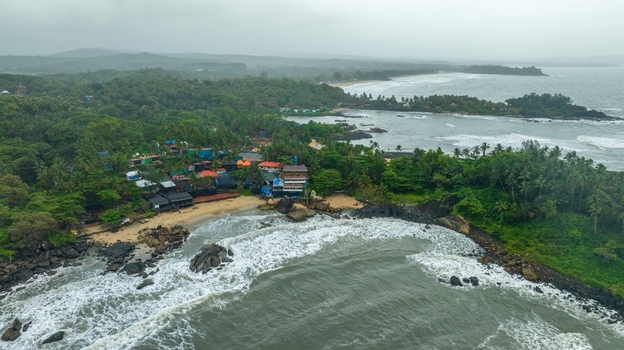 Aerial view of Palolem Beach with lush greenery rocky coastline and small buildings nestled along the shore under a cloudy sky in Canacona Goa India.