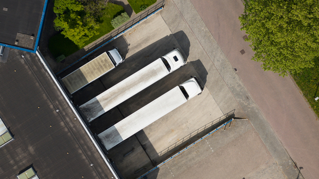 Aerial view of white semi trucks parked at loading docks of an industrial warehouse with green trees and paved roads in Nieuwegein Utrecht Netherlands.