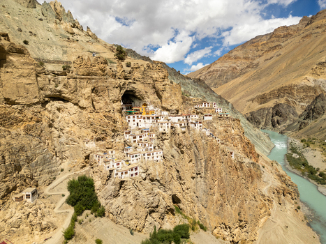 Aerial view of Phukthal Gompa a historic Buddhist monastery built into a cliffside overlooking a turquoise river in a rugged mountain landscape in Phukthal Ladakh India.