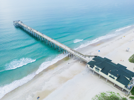 Aerial view of Johnnie Mercers Fishing Pier extending into the turquoise Atlantic Ocean with waves breaking on the sandy beach at Wrightsville Beach North Carolina United States. Aerial view of Johnnie Mercers Fishing Pier extending into the turquoise Atlantic Ocean with waves breaking on the sandy beach at Wrightsville Beach North Carolina United States.