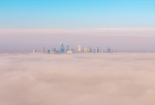 Aerial view of the Warsaw skyline with skyscrapers and the Palace of Culture and Science emerging from a thick layer of pink tinted fog under a clear blue sky in Poland. Aerial view of the Warsaw skyline with skyscrapers and the Palace of Culture and Science emerging from a thick layer of pink tinted fog under a clear blue sky in Poland.