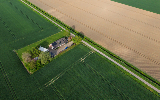 Aerial view of a farmhouse surrounded by lush green crops and plowed brown fields in Vierpolders South Holland Netherlands. Aerial view of a farmhouse surrounded by lush green crops and plowed brown fields in Vierpolders South Holland Netherlands.