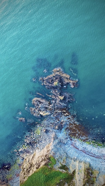 Aerial view of the rugged rocky coastline and turquoise waters of Fishguard Bay with green cliffs and a pebble beach in Fishguard Wales United Kingdom.