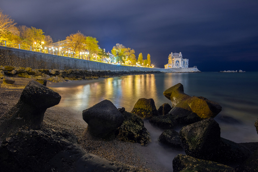 View of the illuminated Constanta Casino at night with rocky breakwaters in the foreground and promenade lights reflecting on the sea in Constanta Judetul Constanta Romania. View of the illuminated Constanta Casino at night with rocky breakwaters in the foreground and promenade lights reflecting on the sea in Constanta Judetul Constanta Romania.