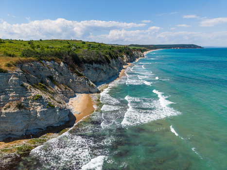 Aerial view of the White Cliffs of Byala featuring rugged limestone formations a sandy beach and turquoise Black Sea waters under a bright blue sky in Byala Varna Bulgaria. Aerial view of the White Cliffs of Byala featuring rugged limestone formations a sandy beach and turquoise Black Sea waters under a bright blue sky in Byala Varna Bulgaria.
